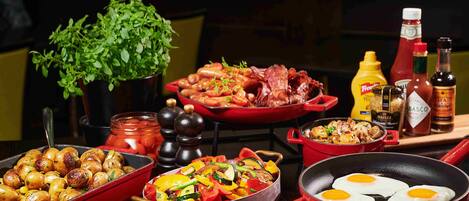 A variety of dishes including roasted potatoes, sautéed vegetables, and eggs in a pan, with condiments and a plant in the background.