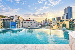Une piscine sur le toit offrant une vue panoramique sur la ville, entourée d’immeubles aux styles architecturaux variés.