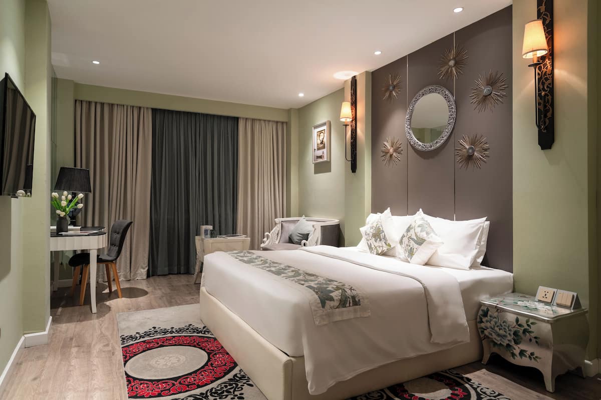 Un dormitorio bien iluminado con una cama grande, mesitas de noche, un escritorio y una silla.