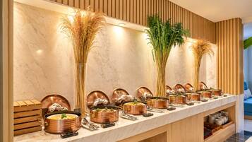 Una larga mesa buffet con fuentes de cobre y altas plantas decorativas.