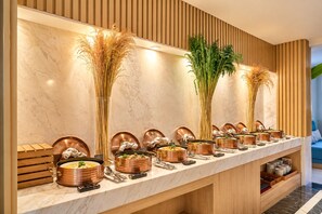 Una larga mesa buffet con fuentes de cobre y altas plantas decorativas.