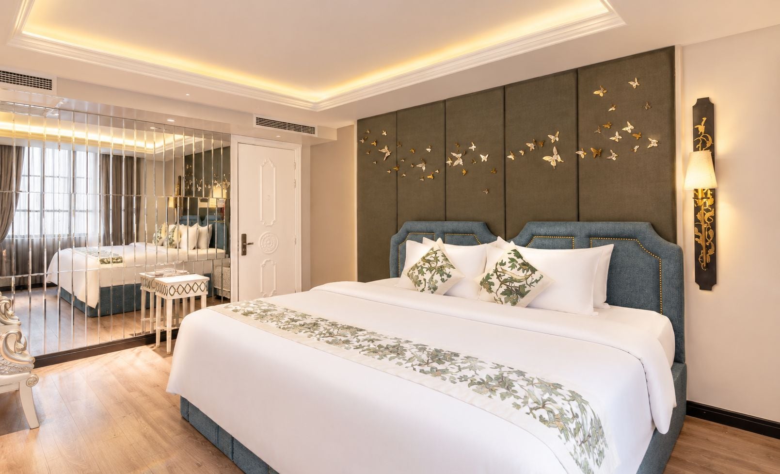 Habitación de hotel con una cama grande, un espejo, una mesita de noche y una pared decorada con motivos de mariposas.