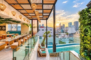 Un restaurant situé sur le toit, offrant une vue sur la ville, doté de balustrades en verre et d’une piscine.