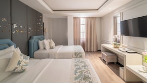 Ein Hotelzimmer mit zwei Betten, einem Schreibtisch, einem Fernseher und einem großen Fenster mit Vorhängen.