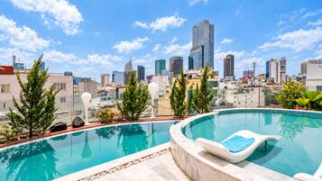 Piscina infinita en la azotea con vista al horizonte de la ciudad, rodeada de plantas en macetas y una silla de descanso.