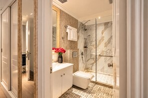 Une salle de bain moderne avec une douche à parois de verre, un mur de douche recouvert de carreaux de marbre, un lavabo blanc et un meuble-lavabo en bois.