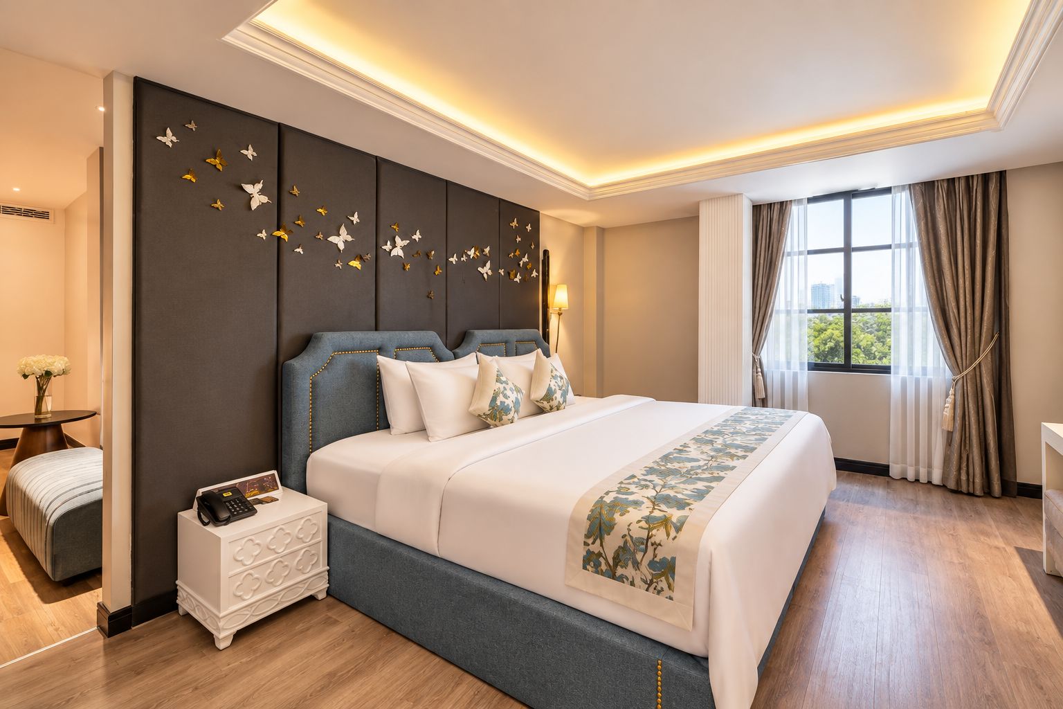 A hotel room with a large bed, a bedside table with a phone, a nightstand, a window with curtains, and a wall with butterfly decorations.