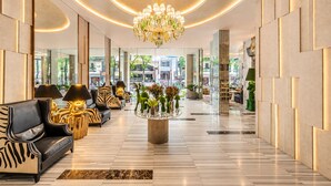Een moderne lobby met een kroonluchter, leren banken, een centrale tafel met planten en uitzicht op buiten.