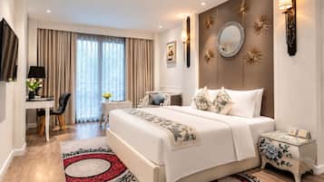 Habitación de hotel con cama, mesitas de noche, escritorio con silla, televisor y ventana grande con cortinas.