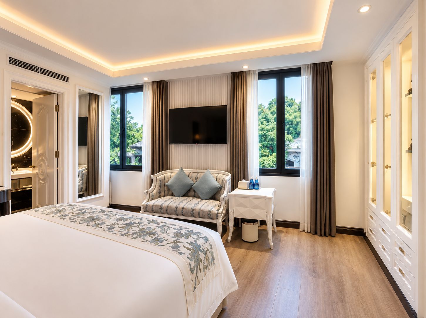 Quarto de hotel com uma cama grande, um sofá, uma TV e vista para o verde lá fora.