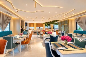 A modern restaurant with a central bar area, multiple dining tables with chairs, and a ceiling with geometric light fixtures.