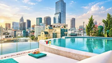 Una piscina en la azotea con vistas a un horizonte urbano, un área de descanso con mesa y sillas, y varios edificios al fondo.