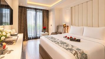 Habitación de hotel con una cama grande, un escritorio con un florero, una silla y una ventana con cortinas.