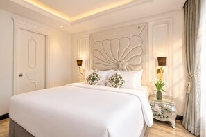 Ein Hotelzimmer mit einem großen Bett, einem verzierten Kopfteil, zwei Nachttischen mit Lampen und einer Tür mit dekorativer Verkleidung.