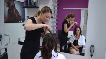Ein Friseursalon mit Spiegel, Regalen für Haarpflegeprodukte und einem sitzenden Kunden.