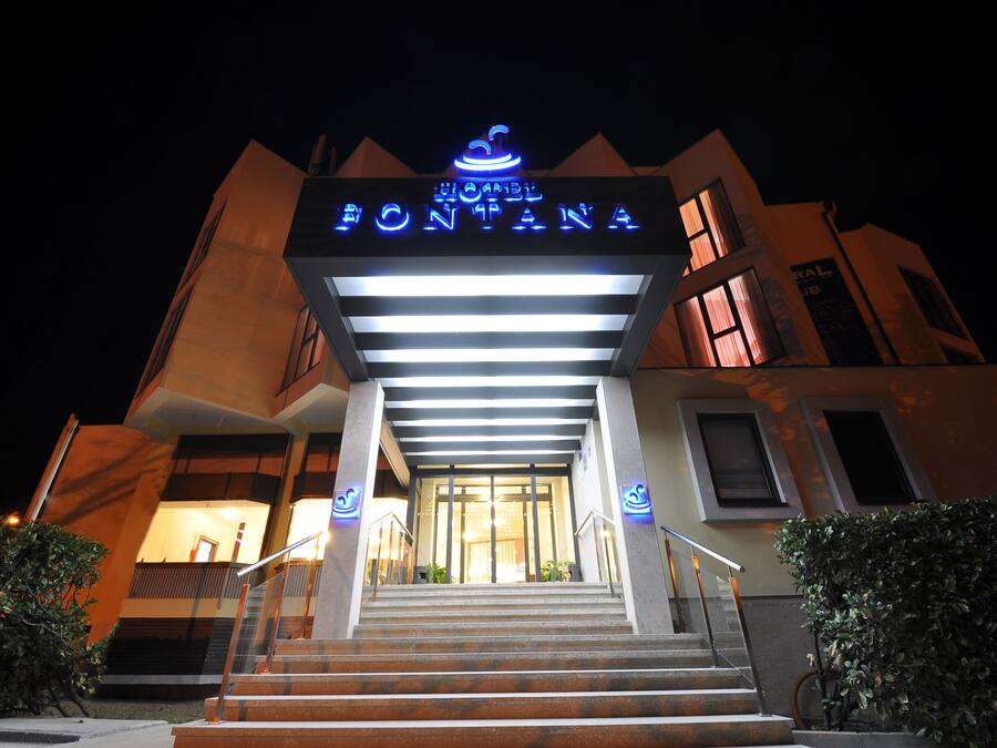 A hotel entrance with a sign reading "Hotel Fontana" and a staircase leading up to the doors.