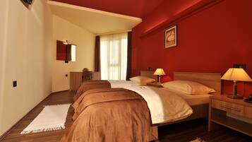 A hotel room with a large bed, two bedside tables, a nightstand, a mirror, and a window with curtains.