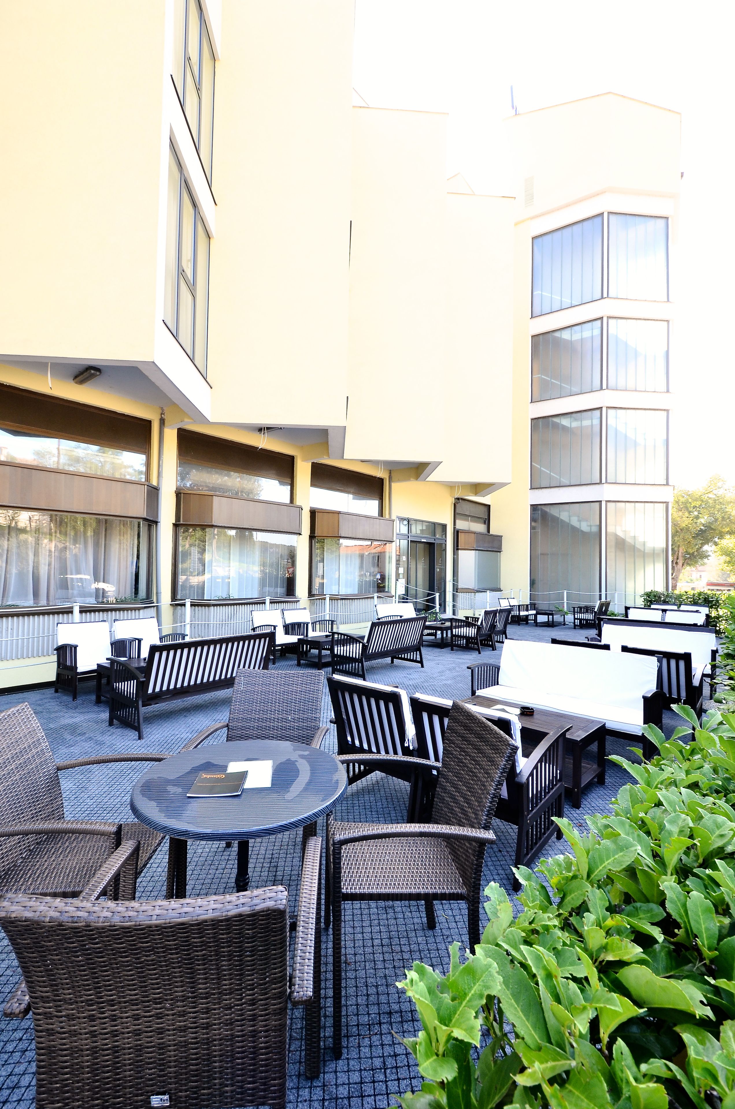 Un patio al aire libre con varias mesas y sillas, ventanas amplias y un edificio de diseño moderno.