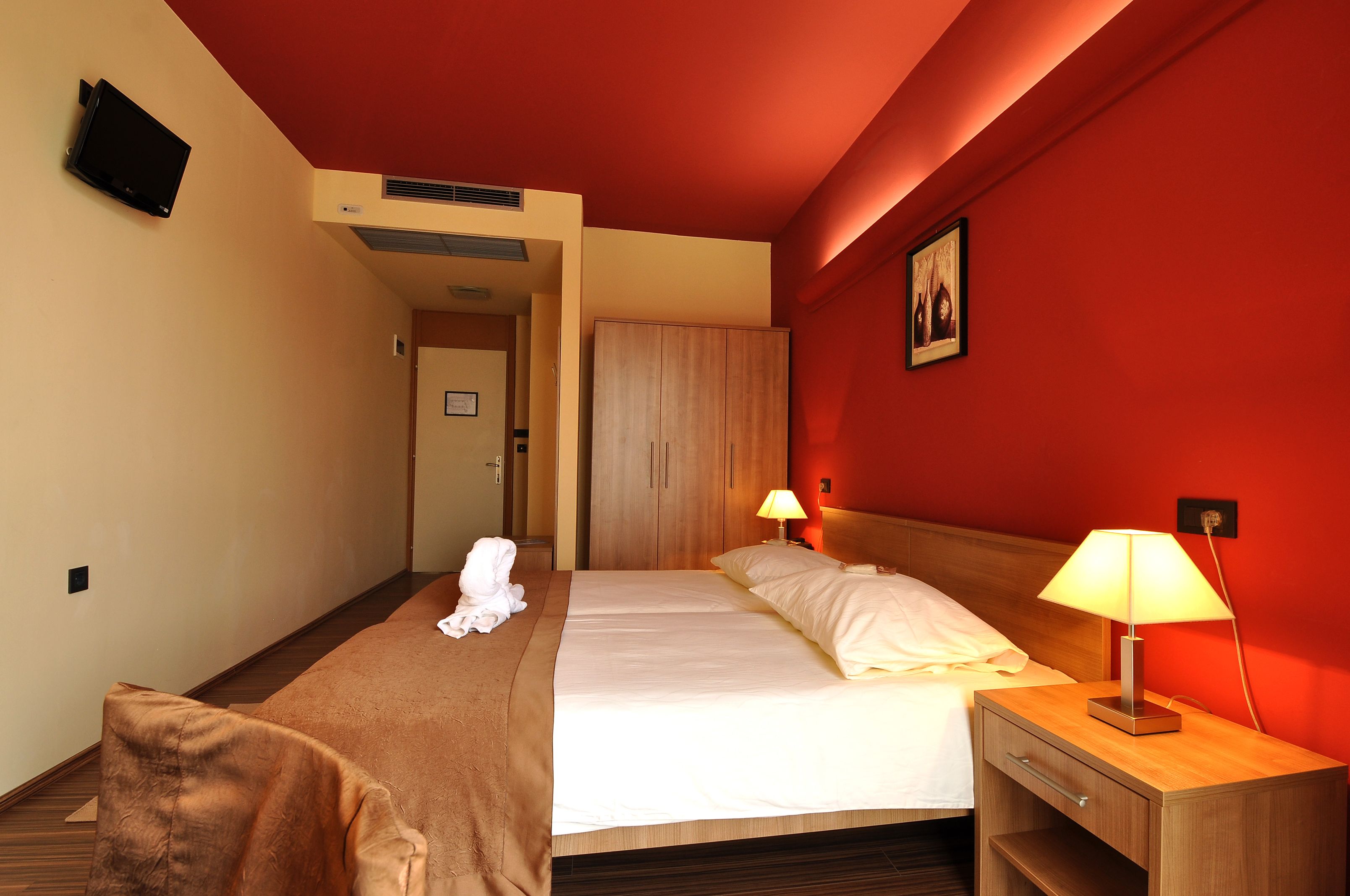 Habitació d'hotel amb un llit, làmpades de nit, un armari de fusta, televisió i una paret vermella.