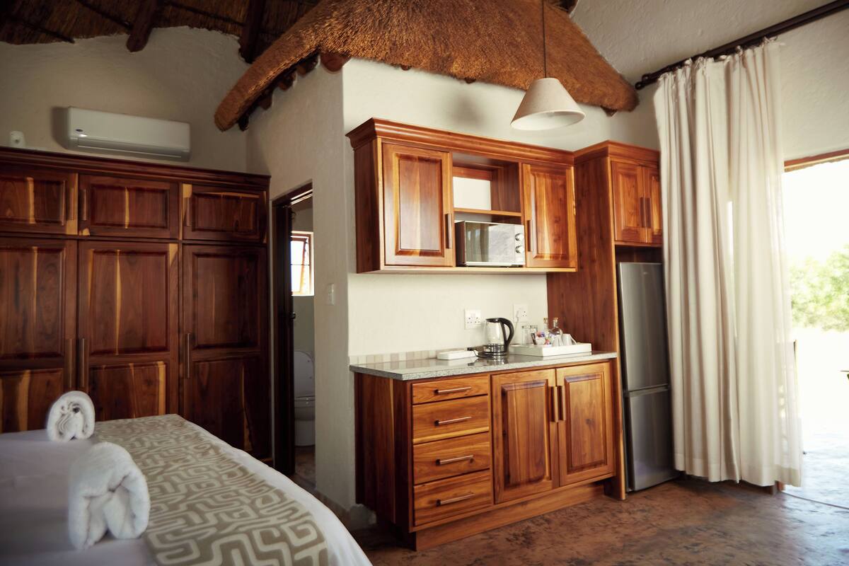 A room with wooden cabinets, a microwave, a refrigerator, and a bed with towels.