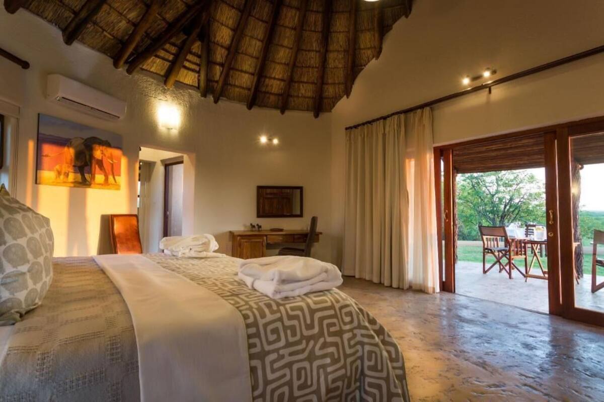 A bedroom with a bed, a desk, a chair, and a view of the outdoors.