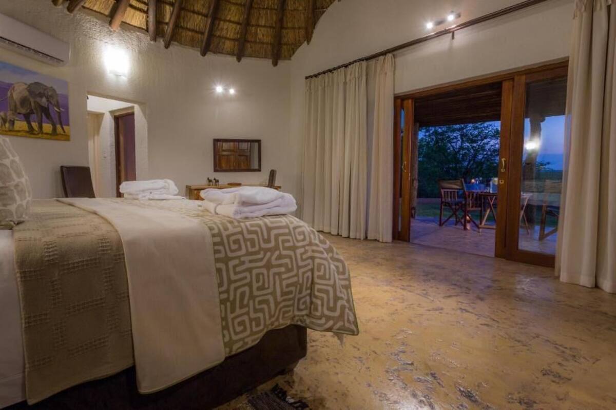 A bedroom with a bed, a nightstand, a painting, and a view of the outdoors.