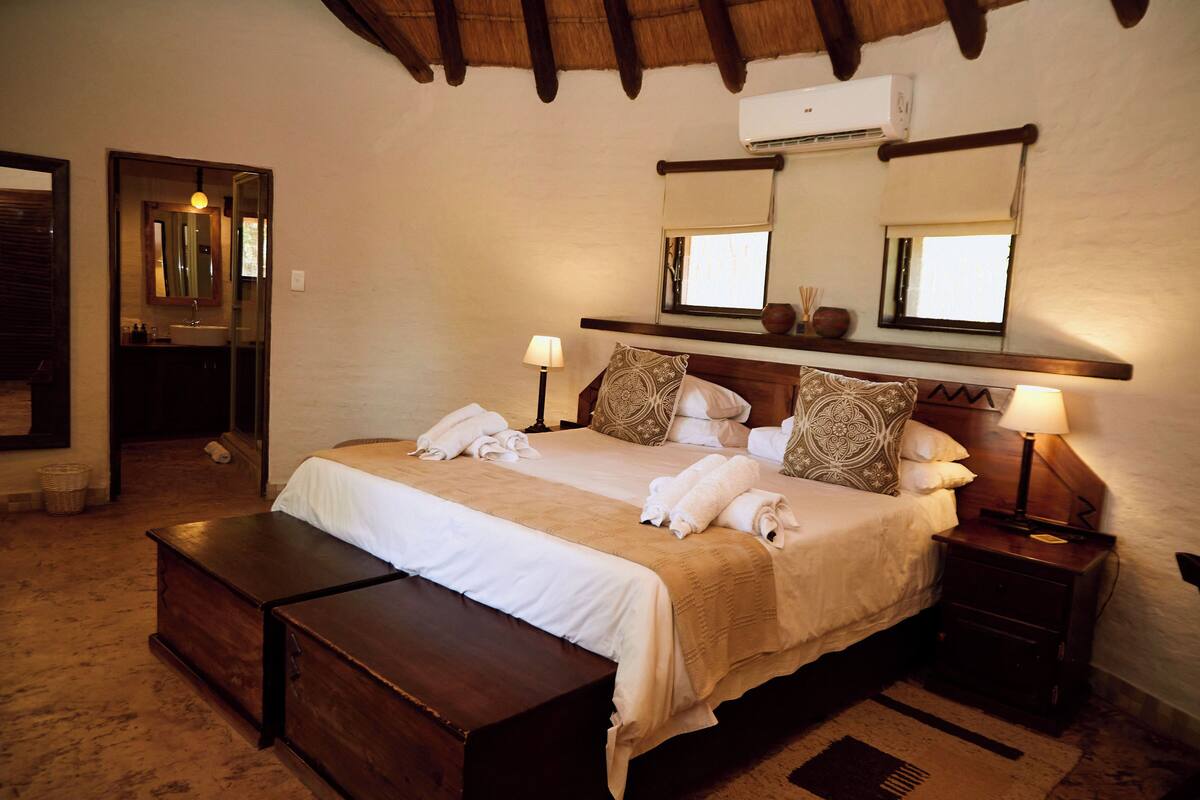 A bedroom with a large bed, bedside lamps, a nightstand, a mirror, and a window with a view.
