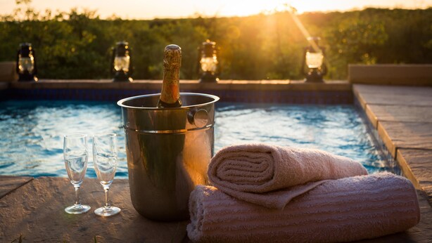 Une scène au bord de la piscine avec une bouteille de champagne, deux verres et une serviette enroulée.