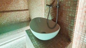 Un baño con un lavamanos grande y redondo, y una zona de ducha con pared de azulejos.