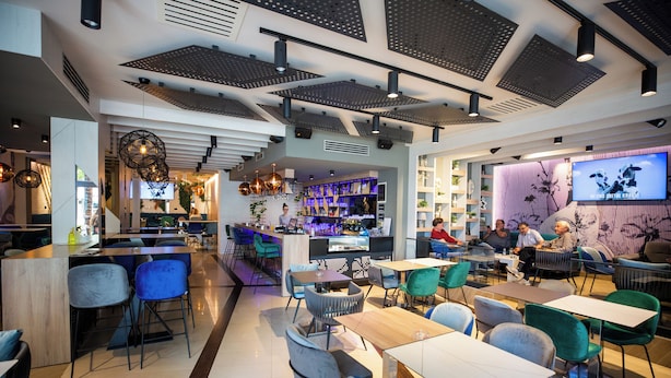 Un restaurante moderno con una zona de bar, asientos y una pantalla de televisión que muestra un programa.
