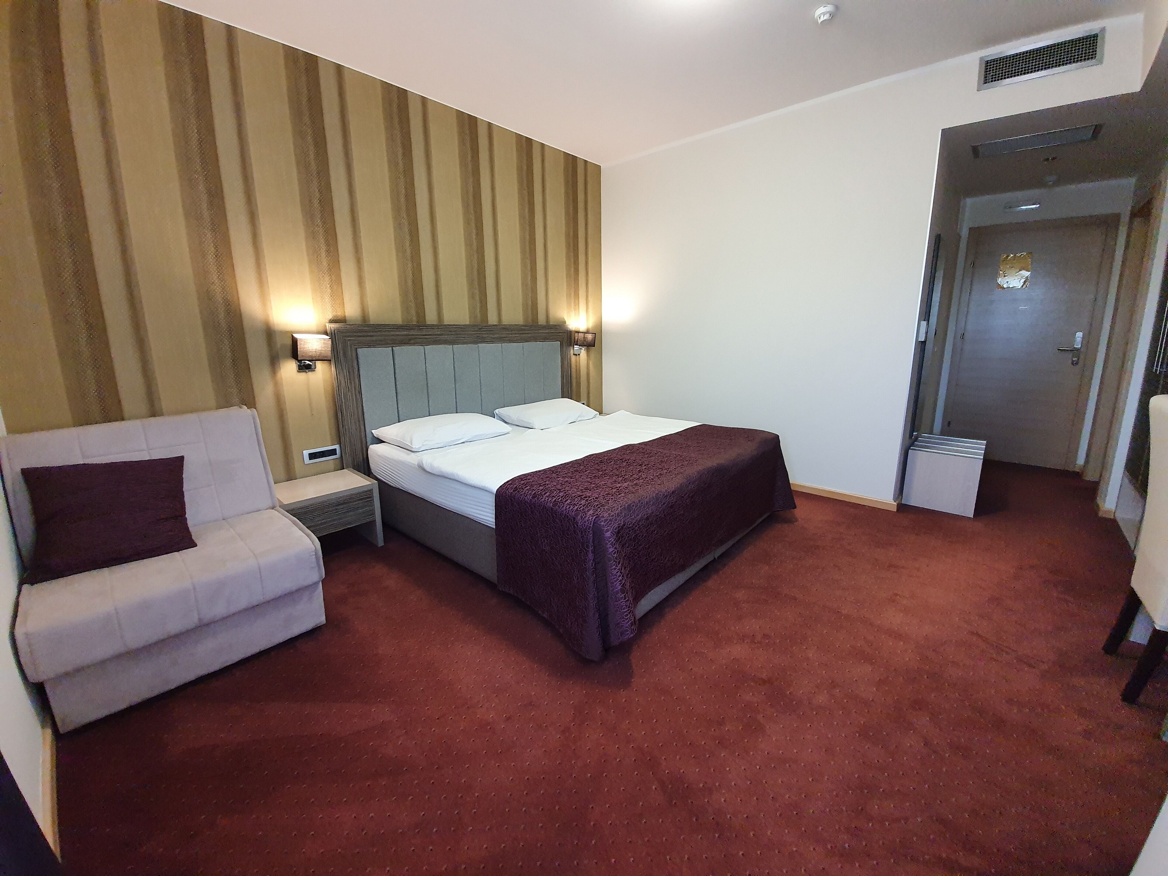 Una camera d'albergo con un letto, un comodino, una sedia e un pavimento rivestito di moquette.