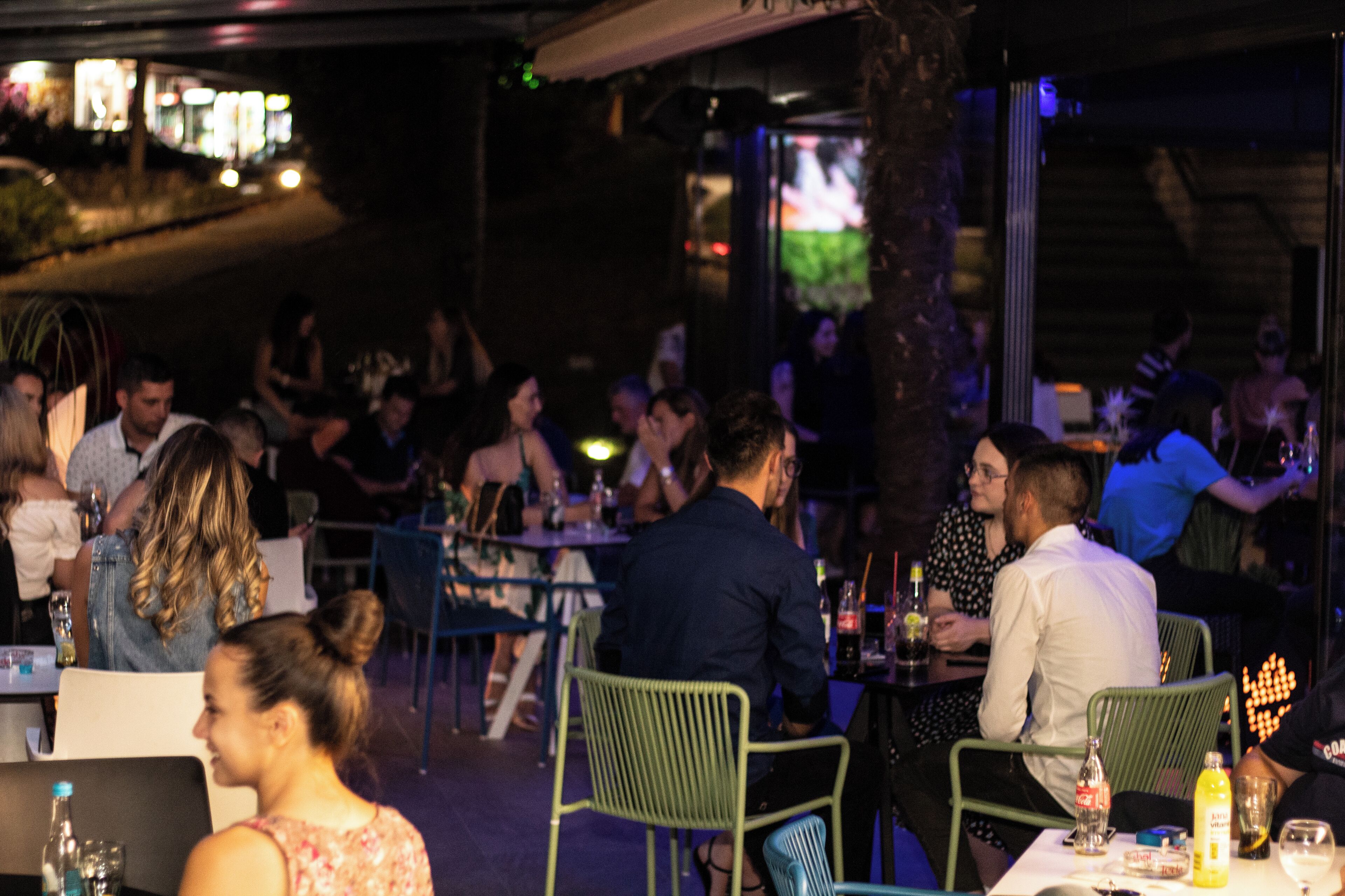 An outdoor dining area with tables and chairs, surrounded by a low wall and trees.