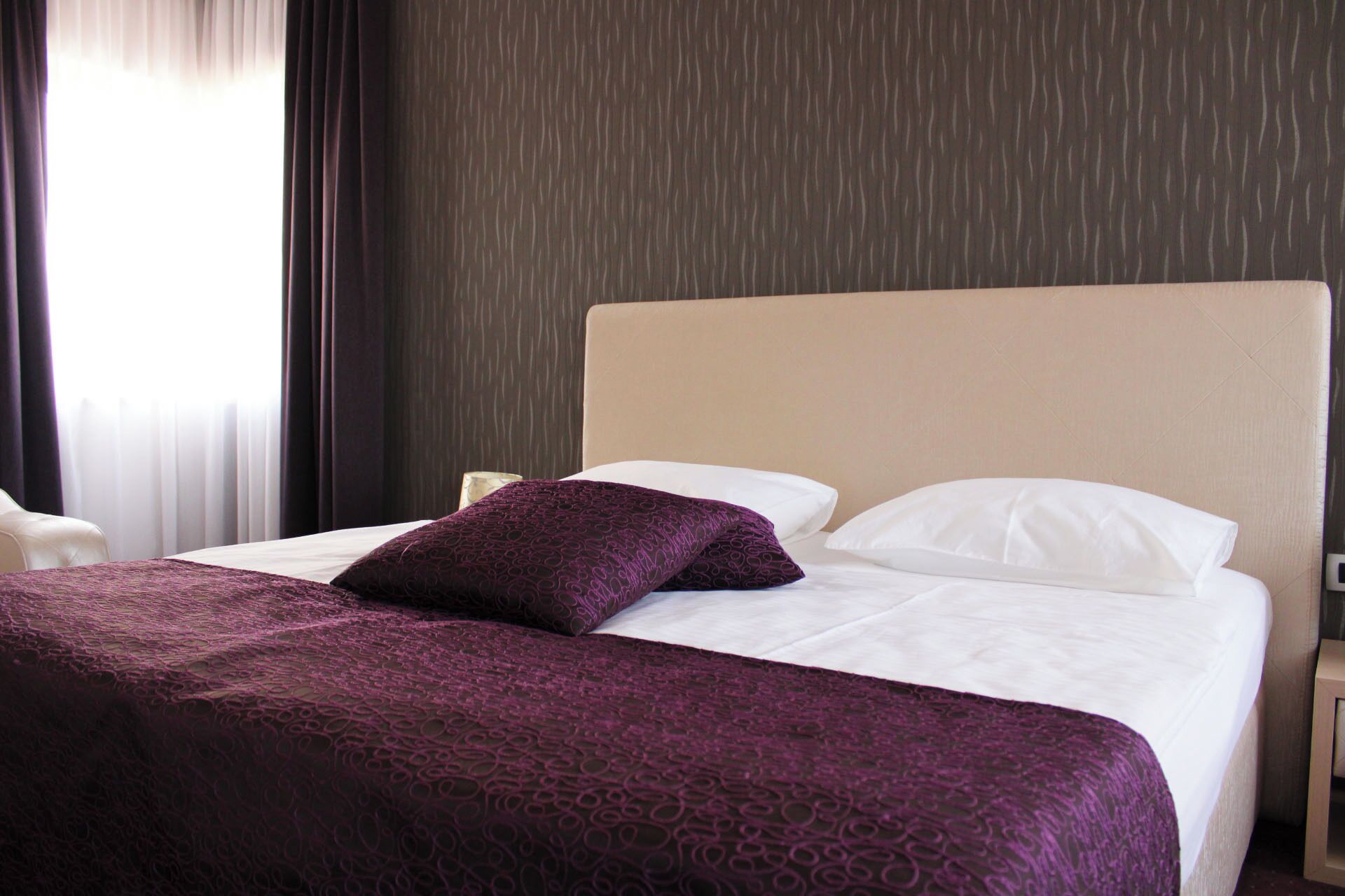 A hotel room with a bed, a headboard, and a window with curtains.