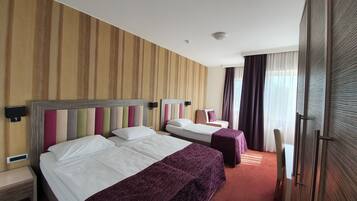 Una habitación de hotel con dos camas, un ventanal con cortinas y una pared con rayas verticales.