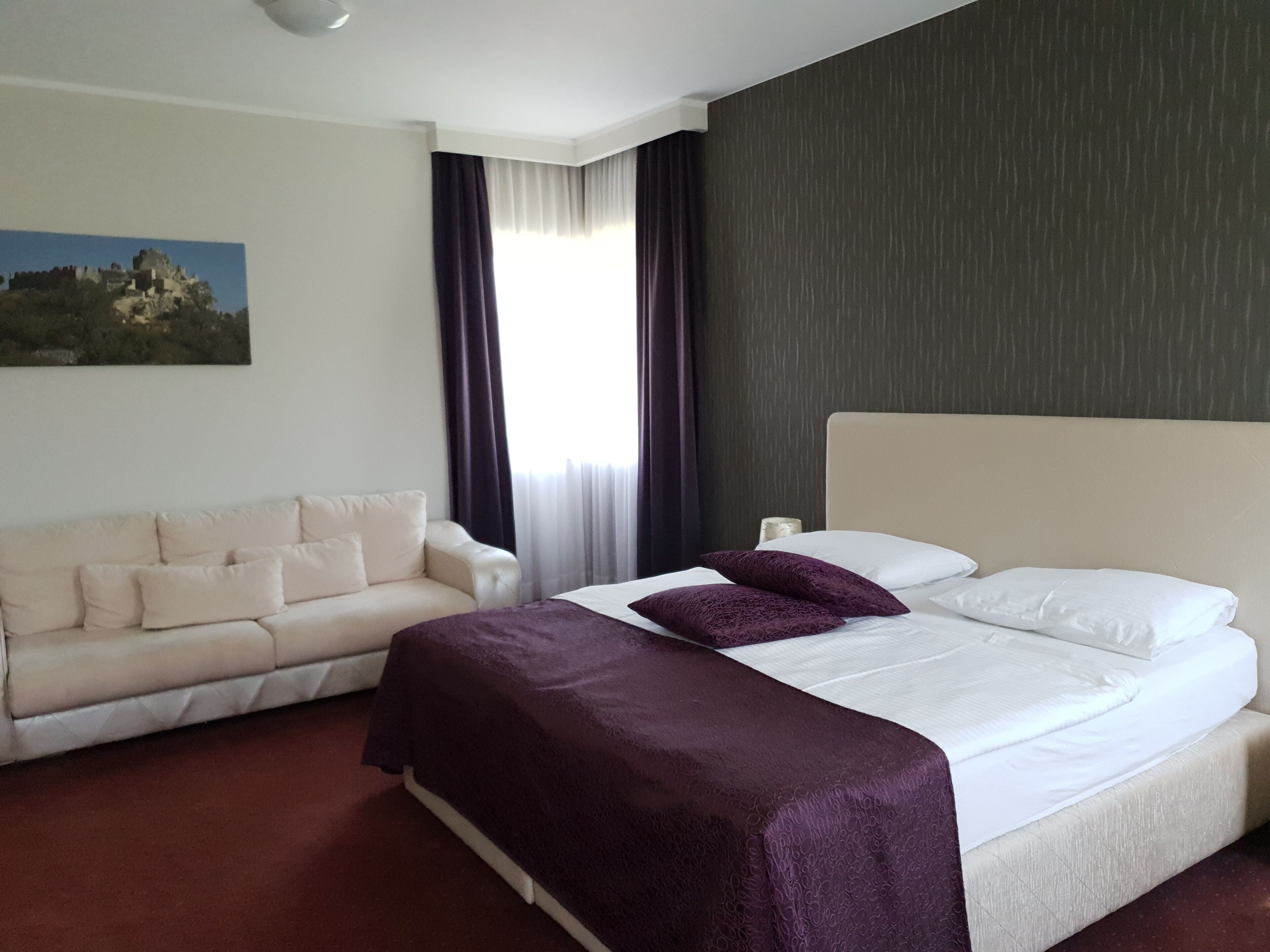 Een hotelkamer met een bed, een bank, een schilderij aan de muur en een raam met gordijnen.
