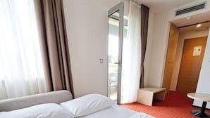 Habitación de hotel con dos camas, una mesita y vistas al exterior.