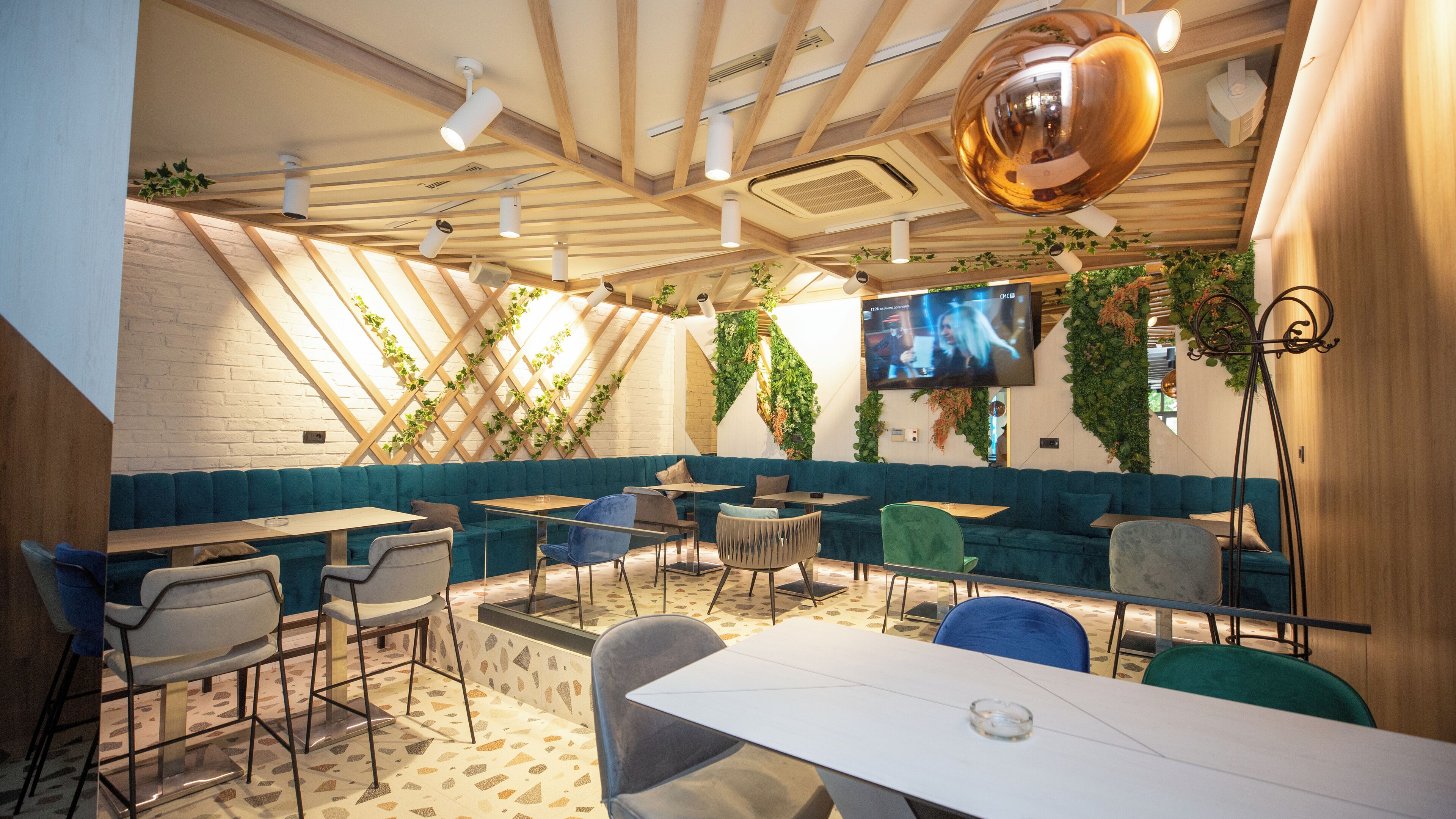 A modern restaurant with a sloped ceiling, green plants, and a large TV screen.