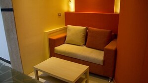 Une petite pièce accueillante, avec un canapé beige, une table basse en bois et un luminaire fixé au mur.