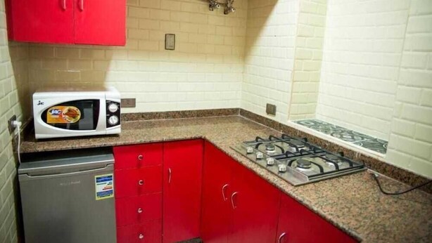 Une cuisine avec des meubles de couleur rouge, un four à micro-ondes blanc, une cuisinière à gaz et un lave-vaisselle.