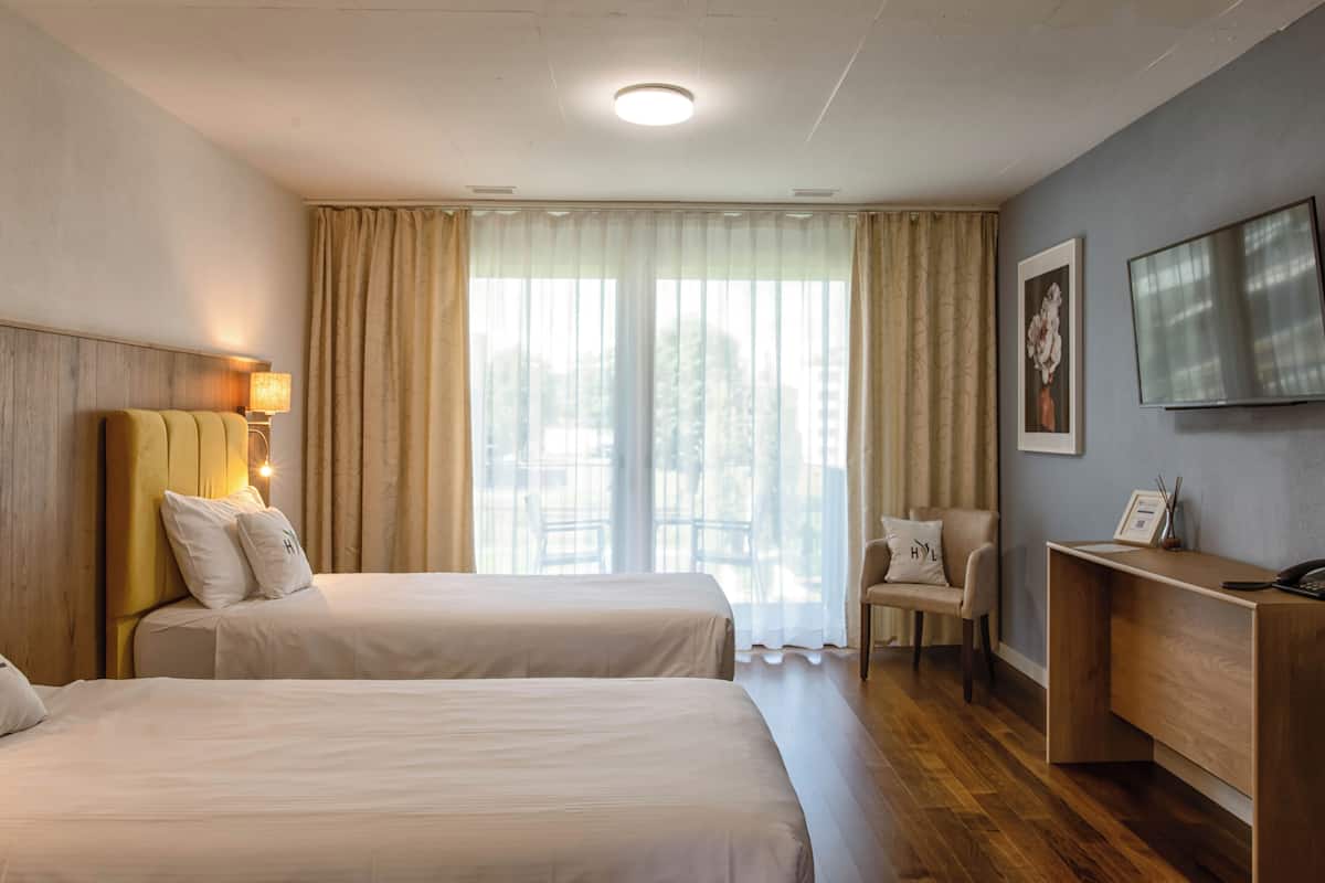 Habitación de hotel con dos camas, un escritorio, una silla, un televisor y una ventana con cortinas.
