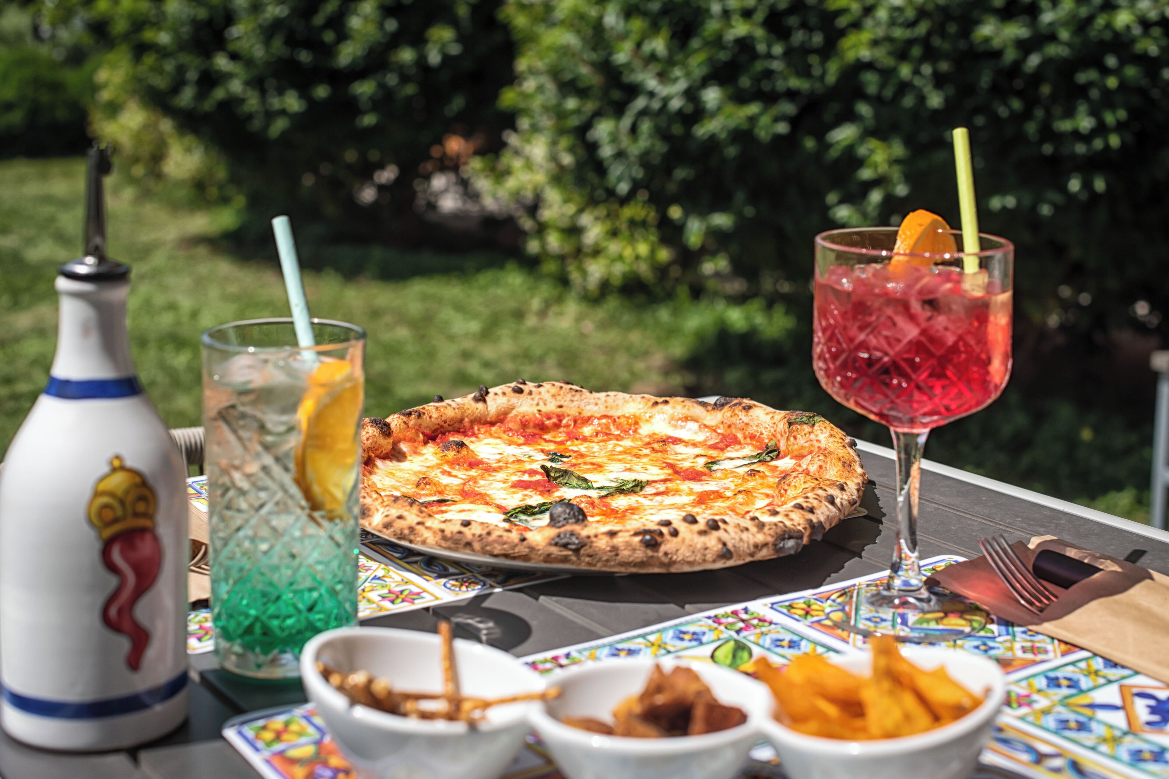 A pizza on a table with a drink and snacks.