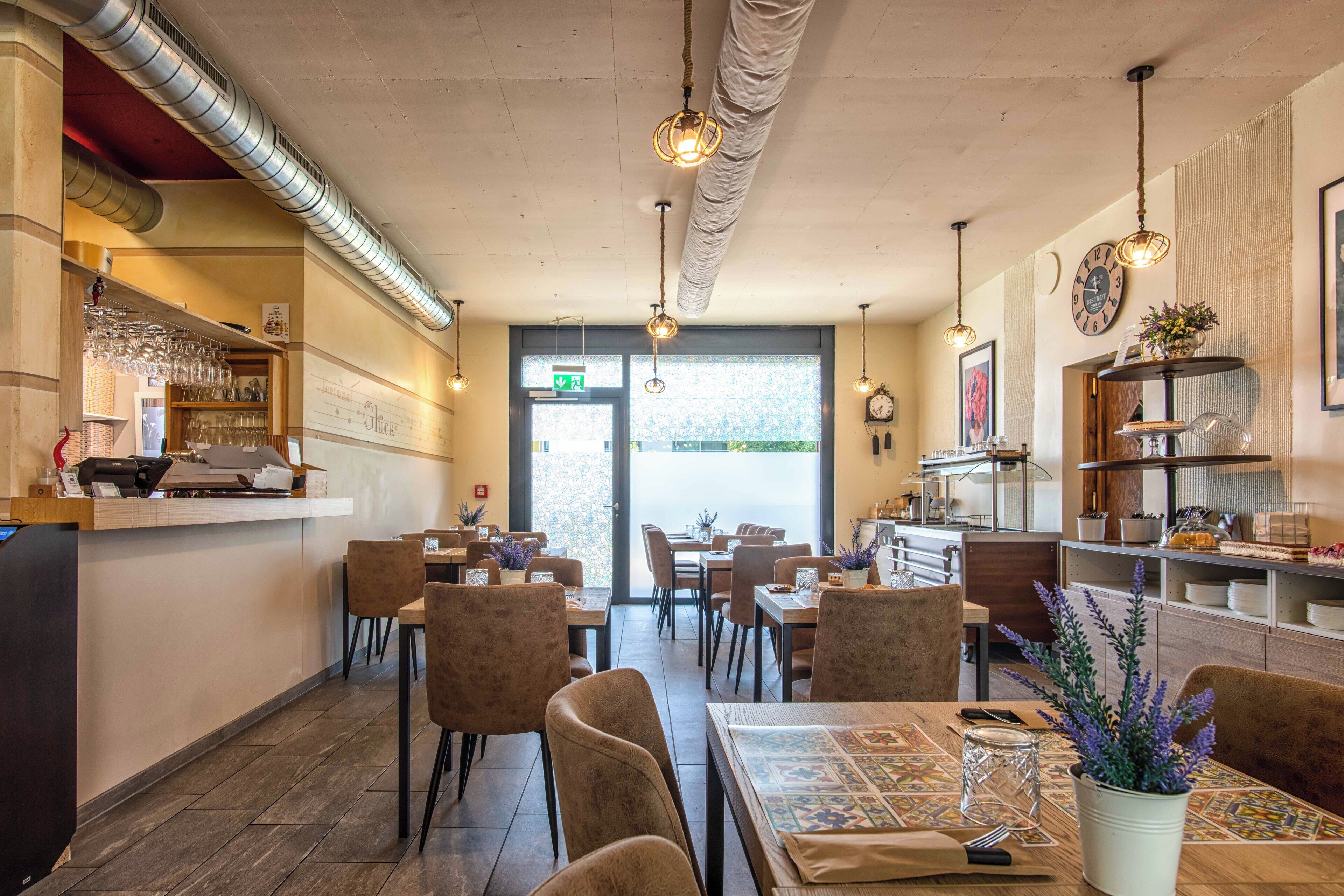 Ein Restaurant mit Bar, mehreren Tischen, Stühlen und hängenden Pendelleuchten.