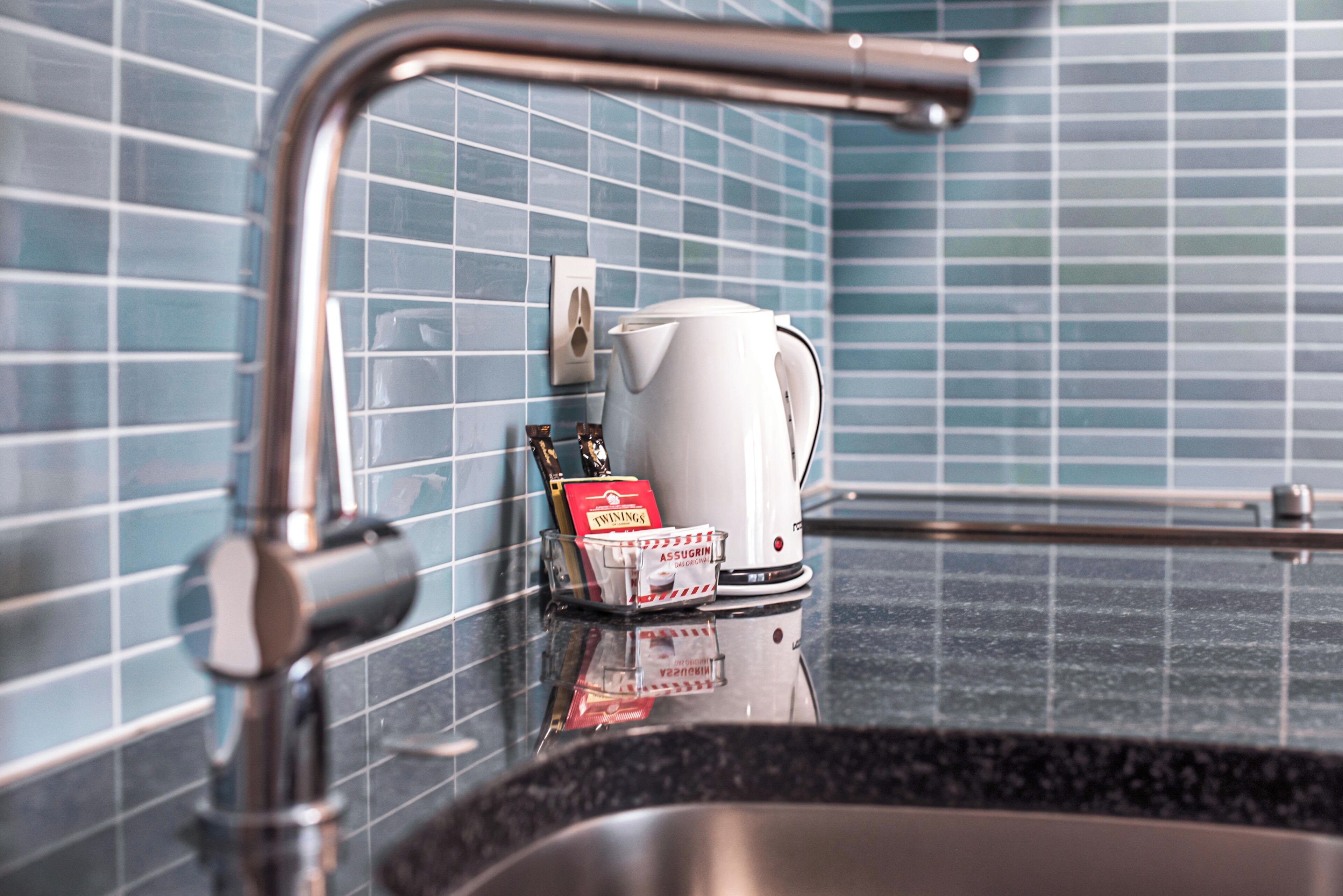 A bathroom with a sink, a white kettle, and a soap dispenser on the counter.