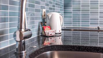 A bathroom with a sink, a white kettle, and a soap dispenser on the counter.