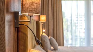 A hotel room with a bed, a wall-mounted lamp, and a window with curtains.