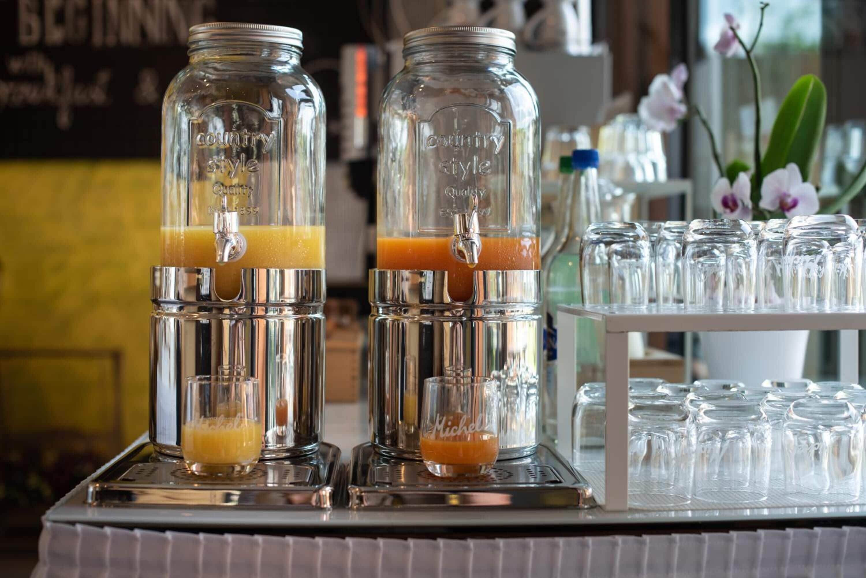 Two glass dispensers with orange juice, a tray with empty glasses, and a sign in the background.