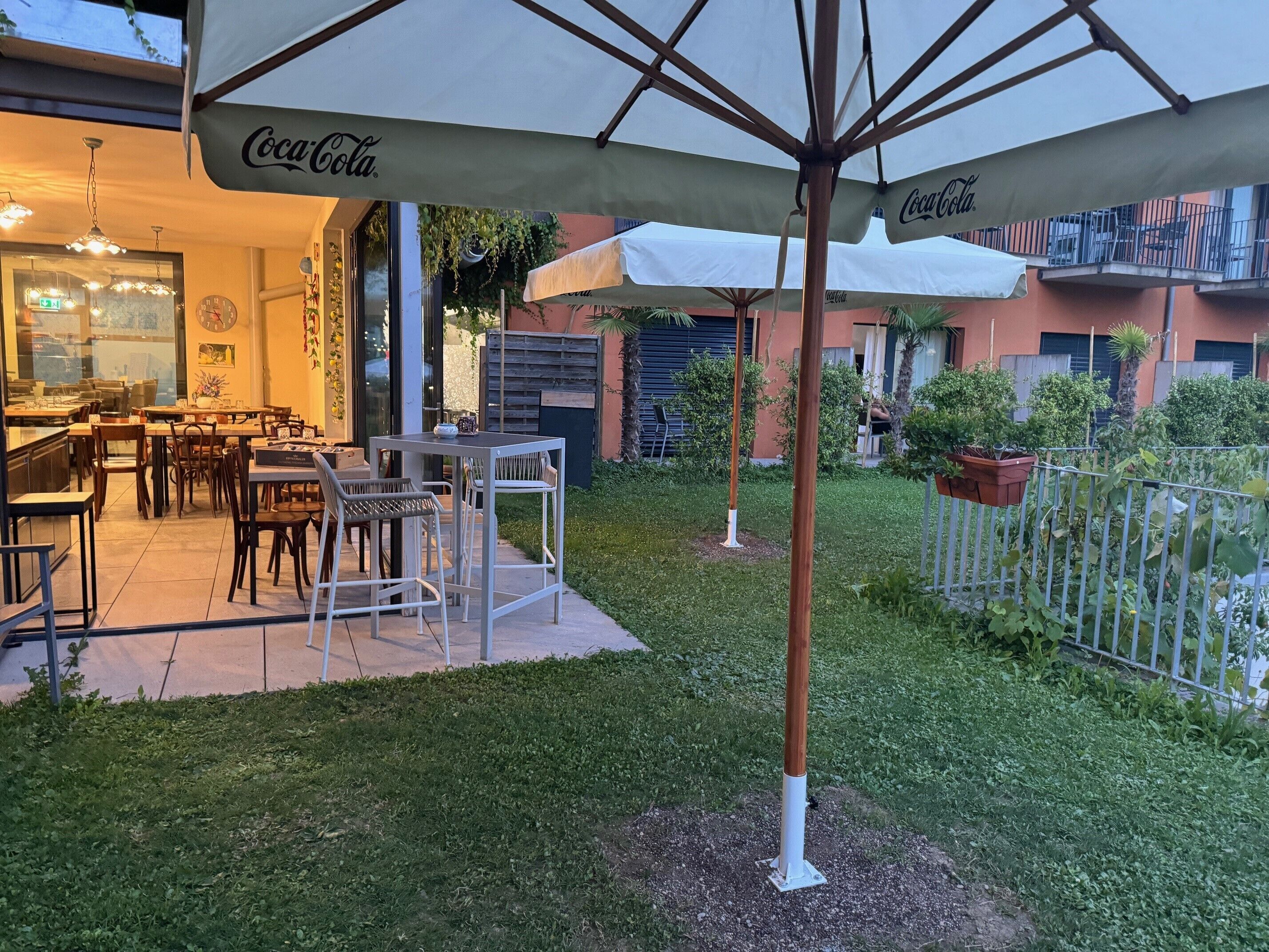 Area esterna con tavolo e sedie sotto ombrelloni con marchio Coca-Cola.
