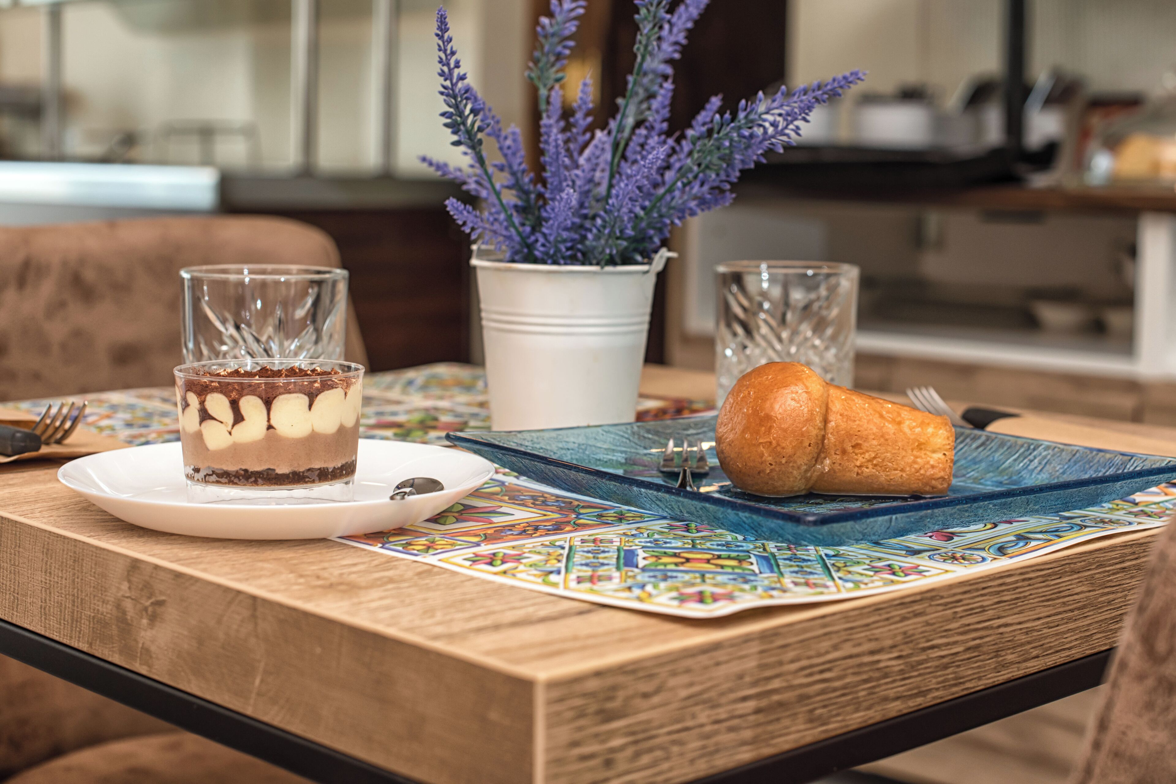 Una mesa de comedor con un postre, una hogaza de pan y un jarrón de lavanda.