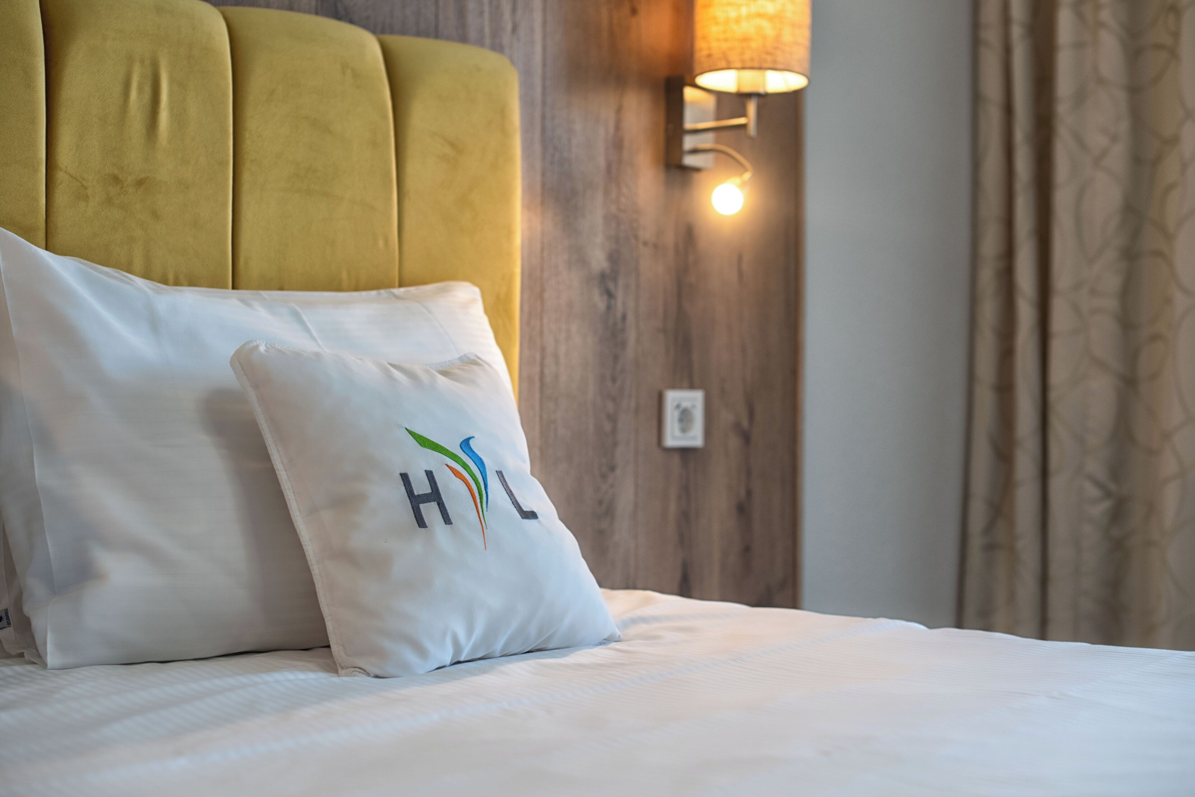 Ein Bett mit einem weißen Kopfkissen, das ein buntes Logo und die Buchstaben "HHL" zeigt.