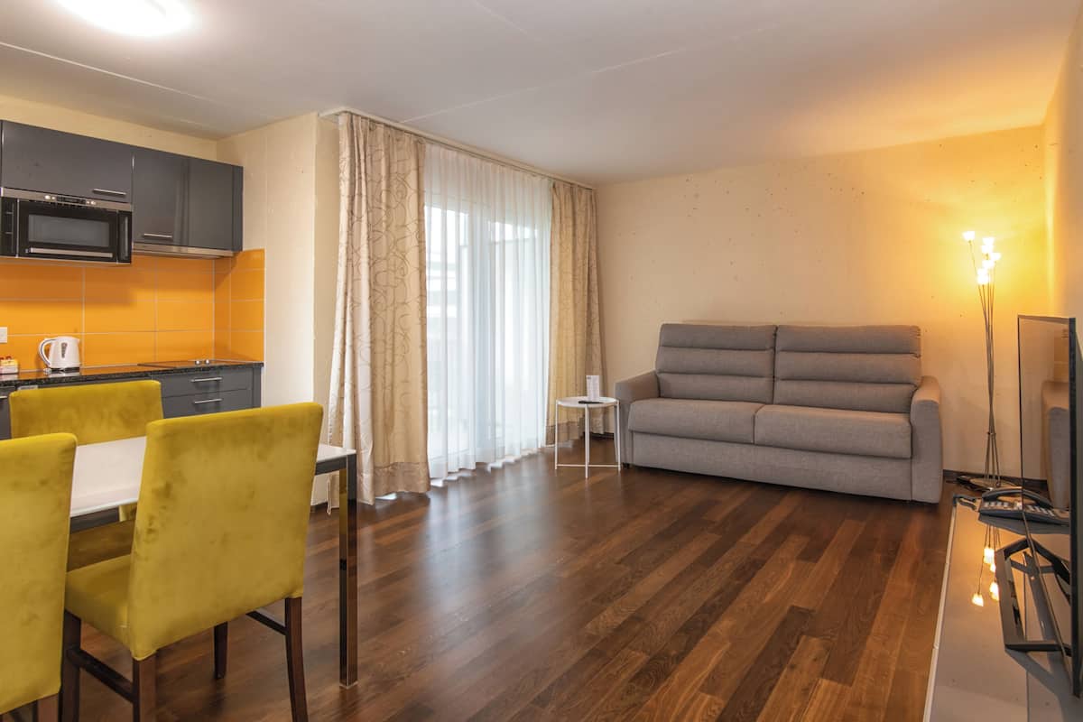 Una sala moderna con un sofá gris, sillas amarillas, una mesa de comedor y una zona de cocina con armarios grises y un microondas.